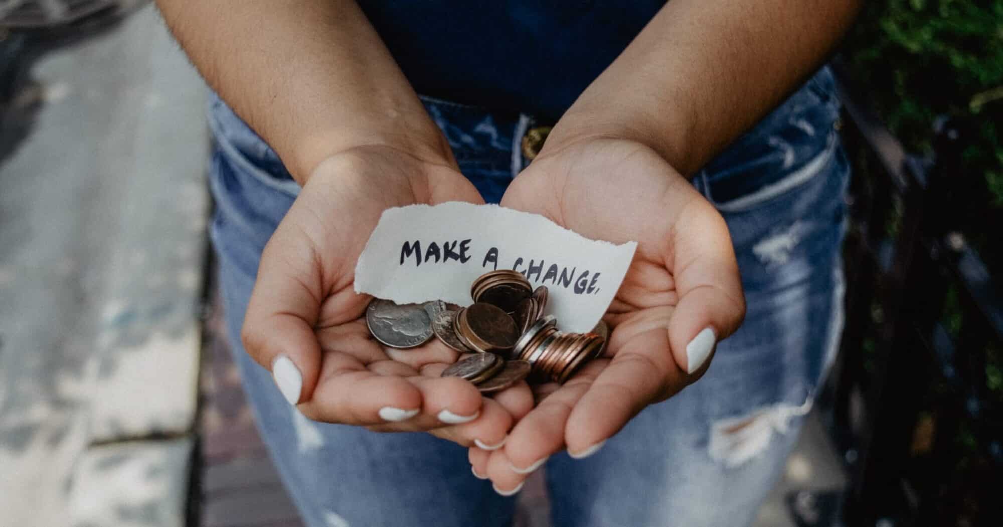 Hands filled with coins and a paper note that reads "make a change."