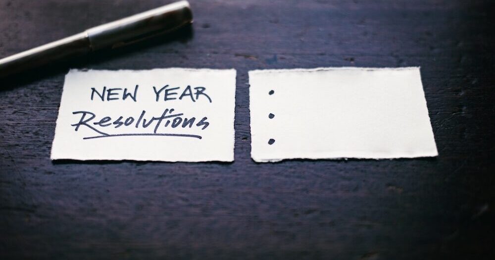 Two pieces of paper, one reads "New Year Resolutions" with resolutions underlined, the other has an empty bulleted list.