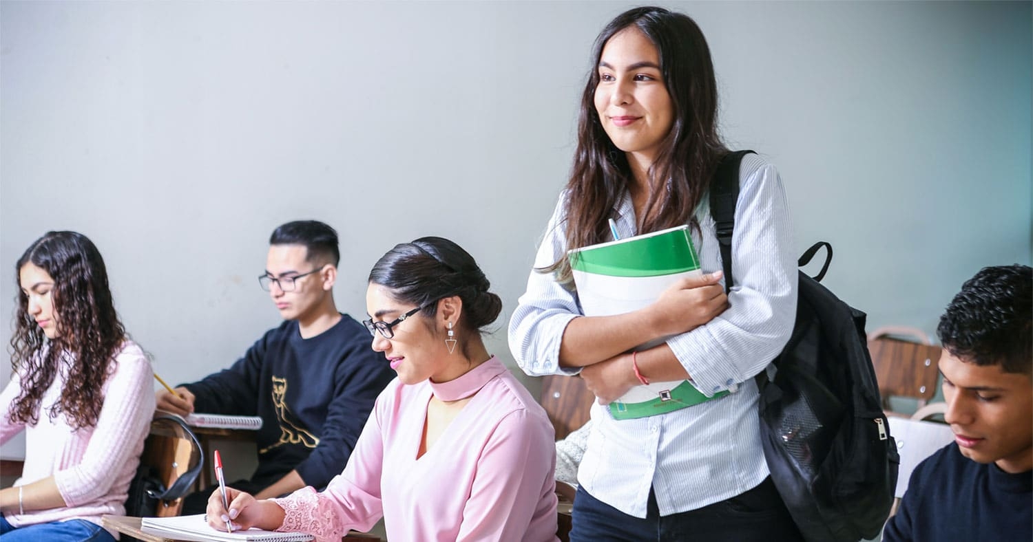 College Students in a class with one student standing up with a smile on her face.